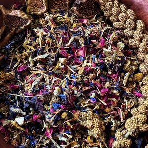 Könnte beinhalten: Nahaufnahme eines Mixes aus getrockneten Kräutern und Blüten, darunter blaue, rosa und gelbe Blütenblätter. Getrocknete Feigen und Samenstände sind ebenfalls zu sehen. Die Zutaten befinden sich in einer Holzschale.