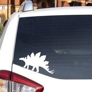 May include: White silhouette of a dinosaur on the rear window of a white car.