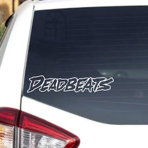 Peut inclure: Autocollant en vinyle blanc avec le mot "Deadbeats" dans une police stylisée sur une vitre de voiture noire.