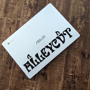 May include: A white ASUS laptop with the word "Alleyevit" in black script. The laptop has a chrome logo in the corner and is on a brown wooden surface.