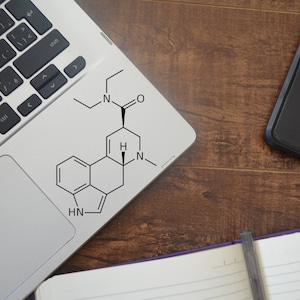 May include: A laptop computer with a white sticker on the touchpad featuring a chemical structure diagram. The diagram includes the letters 'H', 'N', and 'O' and several connected rings.