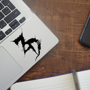 May include: A silver laptop computer with a black graphic sticker on the top of the lid. The sticker is a stylized design of the number 3.
