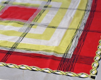 Könnte beinhalten: Eine weiße Tischdecke mit einem geometrischen Muster in Rot, Gelb und Schwarz. Die Tischdecke hat einen seilartigen Rand.
