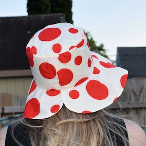 Op de afbeelding: Een witte zonnehoed met rode stippen en een brede rand. De hoed is gemaakt van een lichtgewicht stof en heeft een casual, zomerse stijl.
