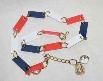 May include: A necklace made of red, white and blue plastic rectangles connected by gold rings. The necklace has a gold chain with a keyhole charm and a clear crystal.