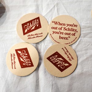 May include: Four round beer coasters with the Schlitz logo in red on a cream background. One coaster features the quote, "When you're out of Schlitz, you're out of beer." The text "The Beer that made Milwaukee Famous" is also present.