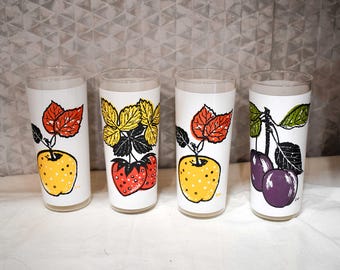 Könnte beinhalten: Vier weiße Glasbecher mit bunten Fruchtmotiven. Jedes Glas zeigt eine andere Frucht: einen Apfel, Erdbeeren, einen Apfel und Pflaumen.