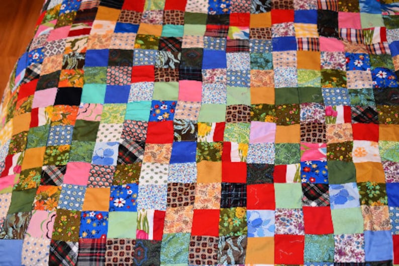 K&ouml;nnte beinhalten: Eine Patchwork-Decke mit einer Vielzahl von Farben und Mustern, darunter Rot, Blau, Gr&uuml;n und Gelb. Die Decke besteht aus Quadraten aus verschiedenen Stoffen, die jeweils ein einzigartiges Design aufweisen.