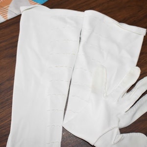 May include: A pair of white long gloves with a stitched design. The gloves are made of a soft, smooth fabric.
