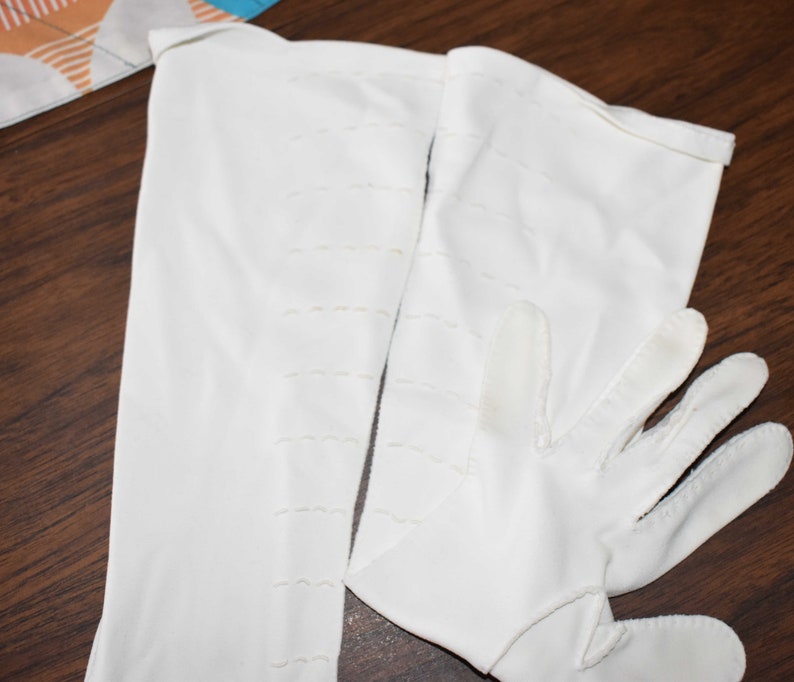 May include: A pair of white long gloves with a stitched design. The gloves are made of a soft, smooth fabric.