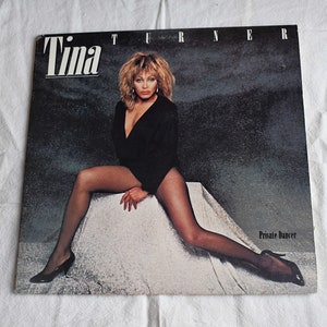 May include: A vinyl record album cover featuring Tina Turner in a black bodysuit and fishnet stockings. The album title "Private Dancer" is printed in white at the bottom right corner.