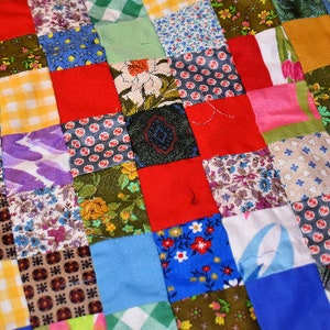 K&ouml;nnte beinhalten: Eine Patchwork-Decke aus verschiedenen bunten Stoffquadraten mit unterschiedlichen Mustern, darunter Blumen, geometrische Muster und Punkte.