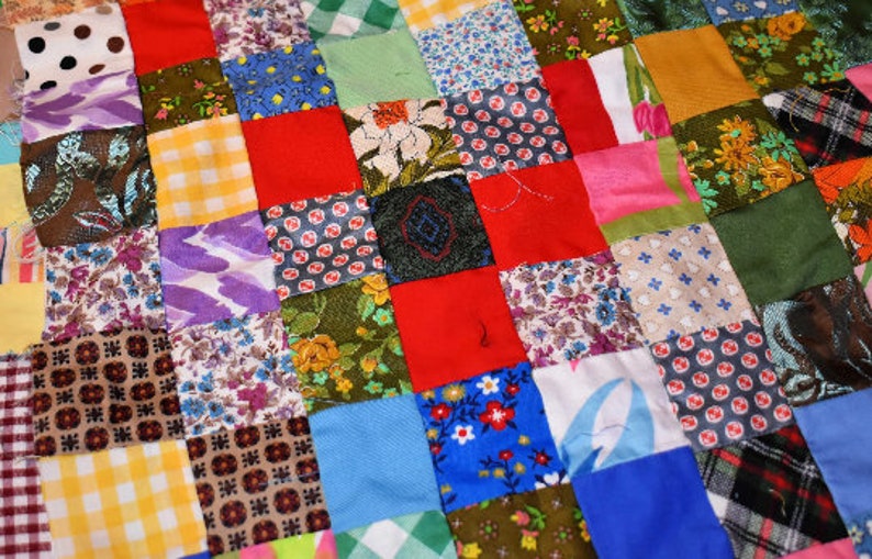 K&ouml;nnte beinhalten: Eine Patchwork-Decke aus verschiedenen bunten Stoffquadraten mit unterschiedlichen Mustern, darunter Blumen, geometrische Muster und Punkte.