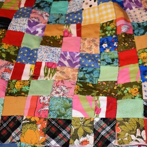 K&ouml;nnte beinhalten: Eine Patchwork-Decke mit einer Vielzahl von bunten Quadraten und Mustern. Die Decke besteht aus verschiedenen Stoffen, darunter Blumenmuster, Karo und einfarbige Stoffe.
