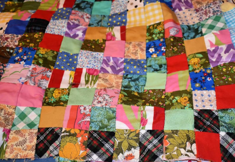 K&ouml;nnte beinhalten: Eine Patchwork-Decke mit einer Vielzahl von bunten Quadraten und Mustern. Die Decke besteht aus verschiedenen Stoffen, darunter Blumenmuster, Karo und einfarbige Stoffe.