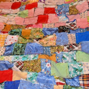 K&ouml;nnte beinhalten: Eine Patchwork-Decke aus verschiedenen Stoffen in unterschiedlichen Farben und Mustern. Die Decke besteht aus Quadraten und Rechtecken aus Stoff, die zusammengen&auml;ht sind.