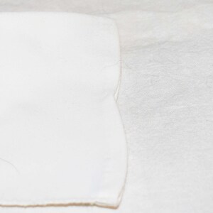 May include: A close-up of two pieces of white fabric, one on top of the other. The top piece of fabric has a slightly curved edge.