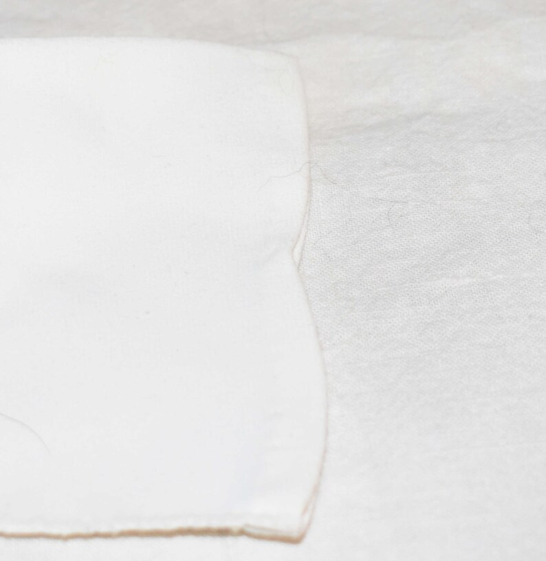 May include: A close-up of two pieces of white fabric, one on top of the other. The top piece of fabric has a slightly curved edge.