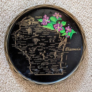 May include: A black metal tray with a gold outline depicting a map of Wisconsin with the names of cities and towns. The tray is decorated with purple violets and green leaves.