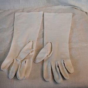 May include: A pair of long, white gloves with fingerless tips. The gloves are made of a smooth, silky fabric.