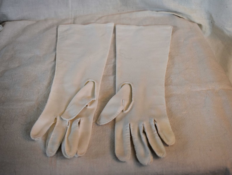 May include: A pair of long, white gloves with fingerless tips. The gloves are made of a smooth, silky fabric.