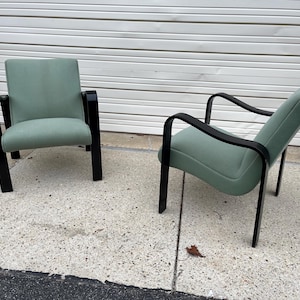 May include: Two mid-century modern chairs with black wood frames and sage green upholstery.