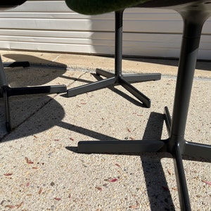 May include: Close-up of the black metal base of three chairs with a star-shaped design. The chairs have green fabric seats.