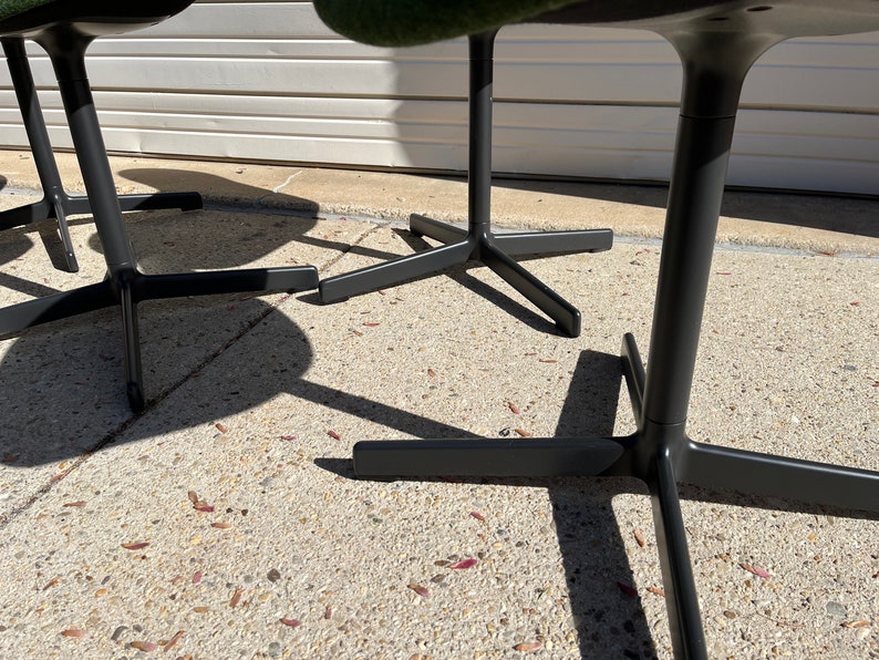 May include: Close-up of the black metal base of three chairs with a star-shaped design. The chairs have green fabric seats.