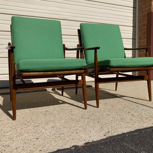 May include: Two mid-century modern chairs with green upholstery and dark wood frames. The chairs are positioned side-by-side on a concrete surface.