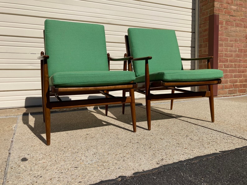 May include: Two mid-century modern chairs with green upholstery and dark wood frames. The chairs are positioned side-by-side on a concrete surface.