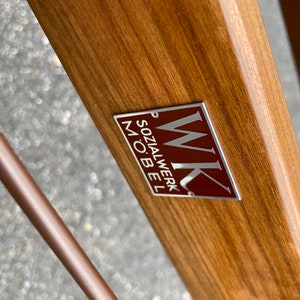 May include: A close-up of a wooden surface with a silver and red metal label that reads "WK Sozialwerk M&ouml;bel".
