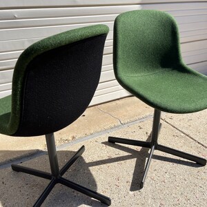 May include: Two green swivel chairs with black metal bases. The chairs are upholstered in a dark green fabric with a black backing.