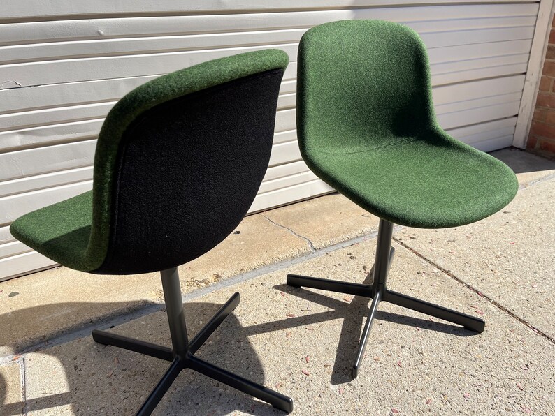 May include: Two green swivel chairs with black metal bases. The chairs are upholstered in a dark green fabric with a black backing.