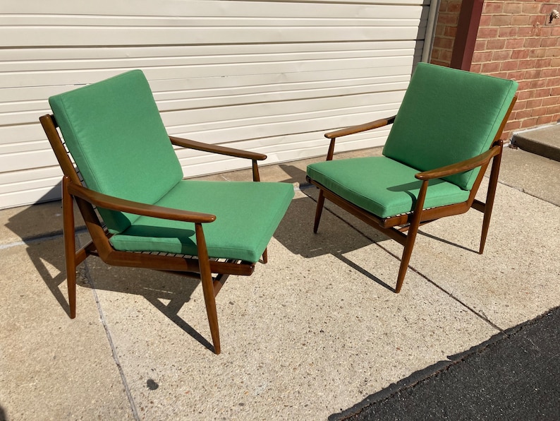 May include: Two mid-century modern chairs with a dark wood frame and green fabric upholstery. The chairs are sitting on a concrete floor.