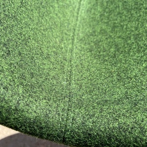 May include: Close-up of a green fabric with a subtle texture. The fabric has a seam running down the center.