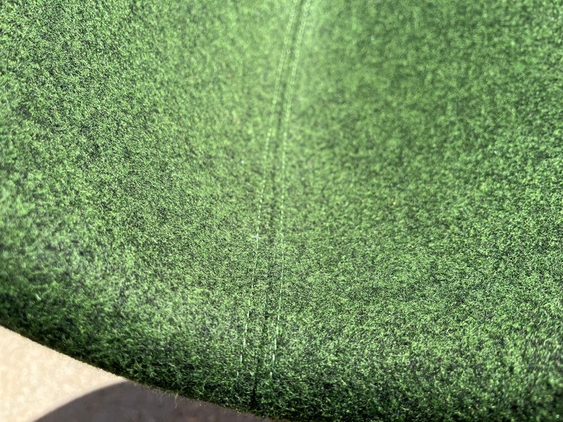 May include: Close-up of a green fabric with a subtle texture. The fabric has a seam running down the center.