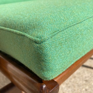 May include: Close-up of a green upholstered chair with a wooden frame. The chair has a tufted seat and a simple design.