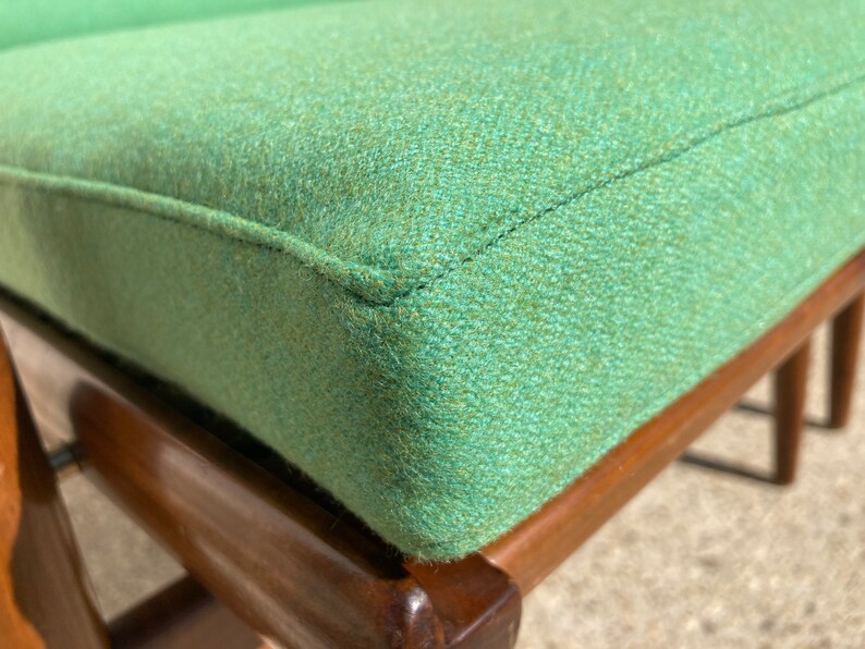 May include: Close-up of a green upholstered chair with a wooden frame. The chair has a tufted seat and a simple design.