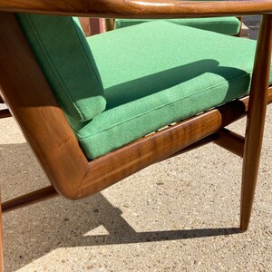 May include: A green upholstered armchair with a wooden frame. The chair has a high back and a wide seat. The chair is made of solid wood and has a simple, elegant design.