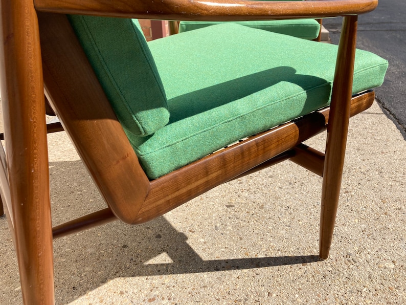 May include: A green upholstered armchair with a wooden frame. The chair has a high back and a wide seat. The chair is made of solid wood and has a simple, elegant design.