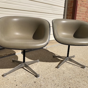 May include: Two gray swivel chairs with a star-shaped base. The chairs are made of molded plastic and have a smooth, rounded design.