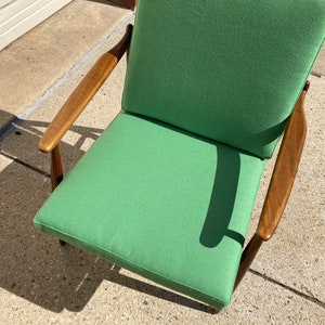 May include: A green upholstered armchair with wooden arms and legs. The chair is sitting on a concrete surface.
