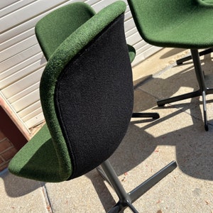 May include: Four green swivel chairs with black metal bases. The chairs have a black fabric back and a green fabric seat.