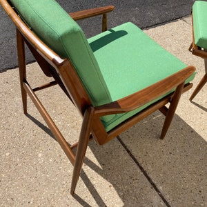 May include: A green upholstered armchair with a wooden frame. The chair has a simple, mid-century modern design.