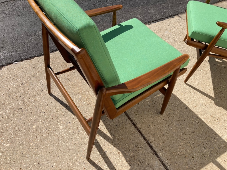 May include: A green upholstered armchair with a wooden frame. The chair has a simple, mid-century modern design.