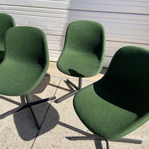 May include: Four dark green upholstered chairs with black metal legs. The chairs are arranged in a row, facing the viewer.