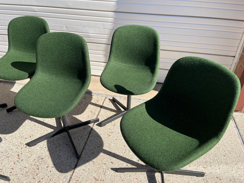 May include: Four dark green upholstered chairs with black metal legs. The chairs are arranged in a row, facing the viewer.