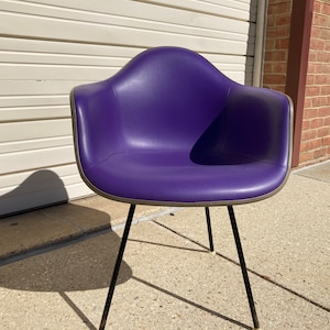 May include: A purple chair with black metal legs. The chair is made of molded plastic and has a slight sheen.