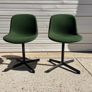 May include: Two dark green swivel chairs with black metal bases. The chairs are on a concrete surface.