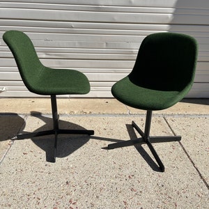 May include: Two dark green swivel chairs with black metal bases. The chairs are on a gray concrete surface.